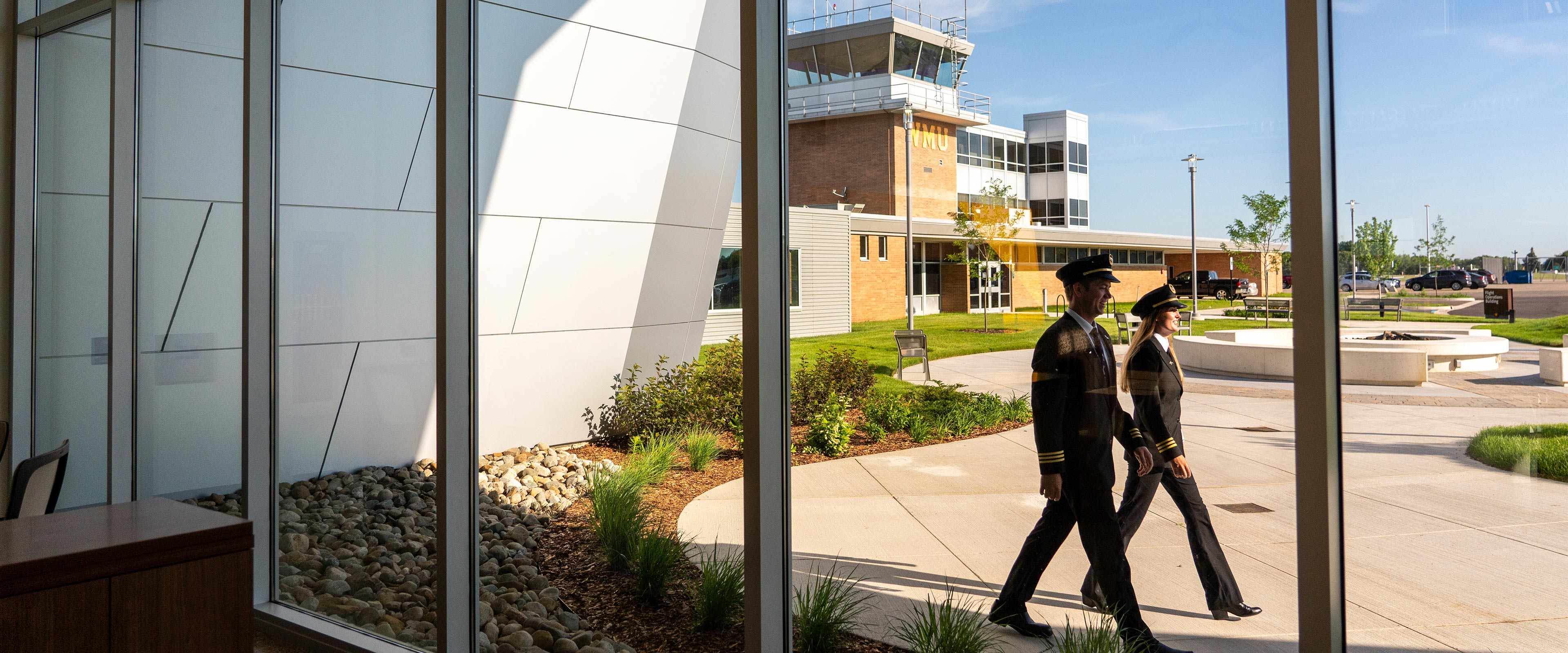 Two pilots walk outside the windows of WMU's Aviation Education Center.