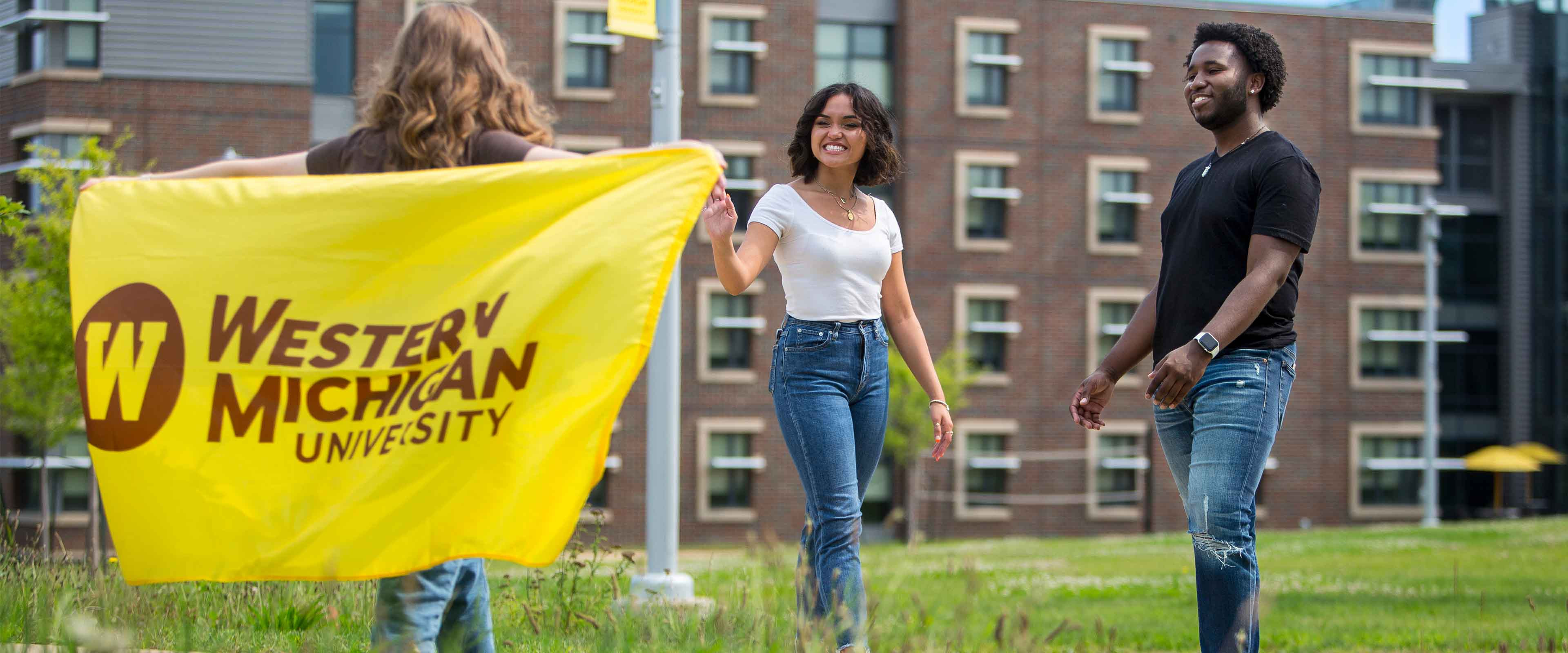Three students outside on campus with a WMU flag.