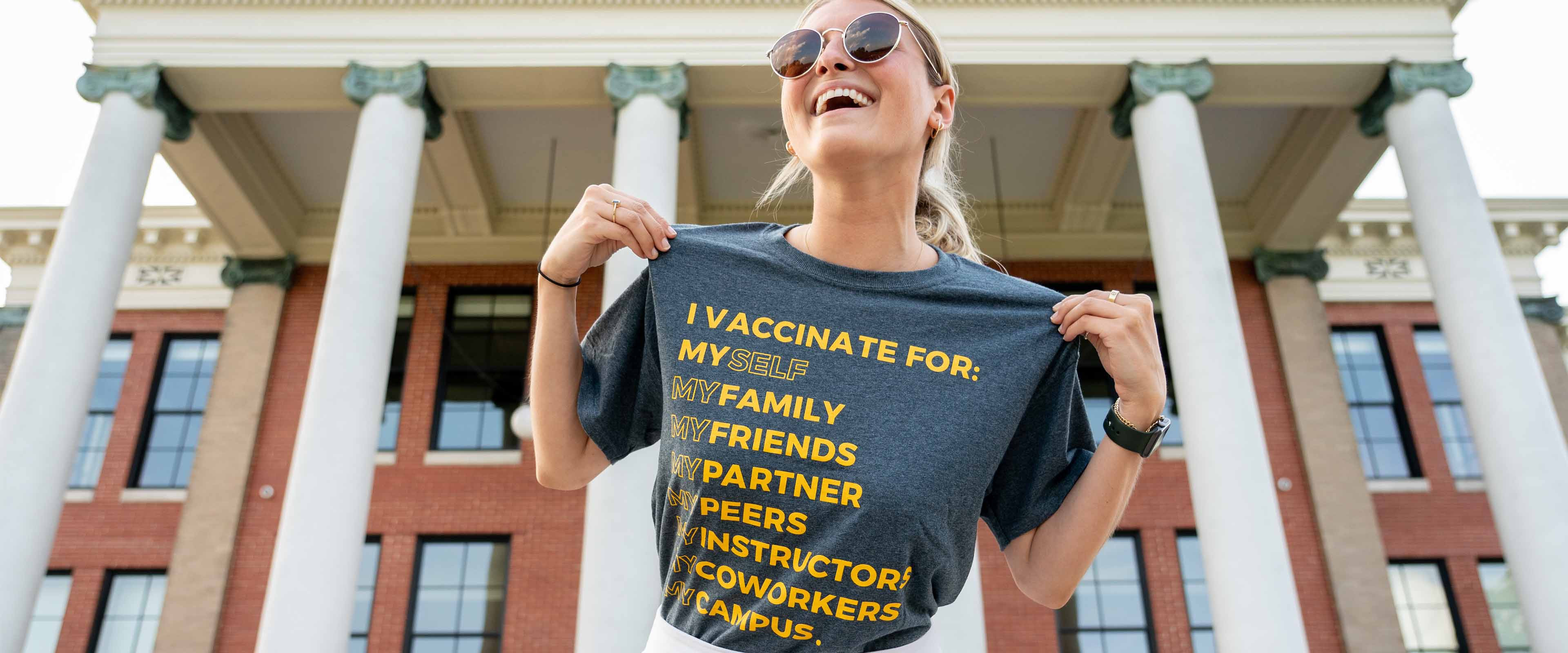 A woman wearing a shirt that reads, "I vaccinate for: My self, my family, my friends, my partner, my peers, my instructors, my coworkers, my campus.