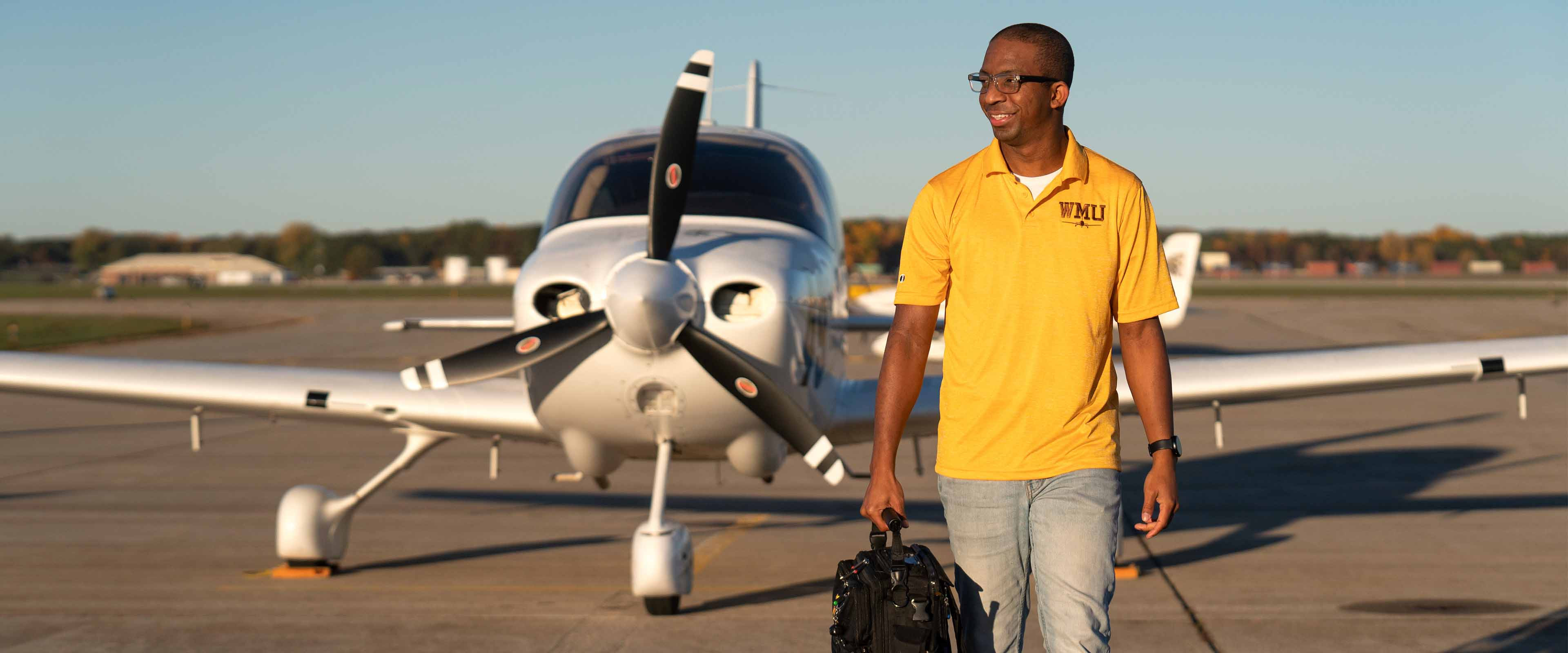 A student walking in front of an airplane.