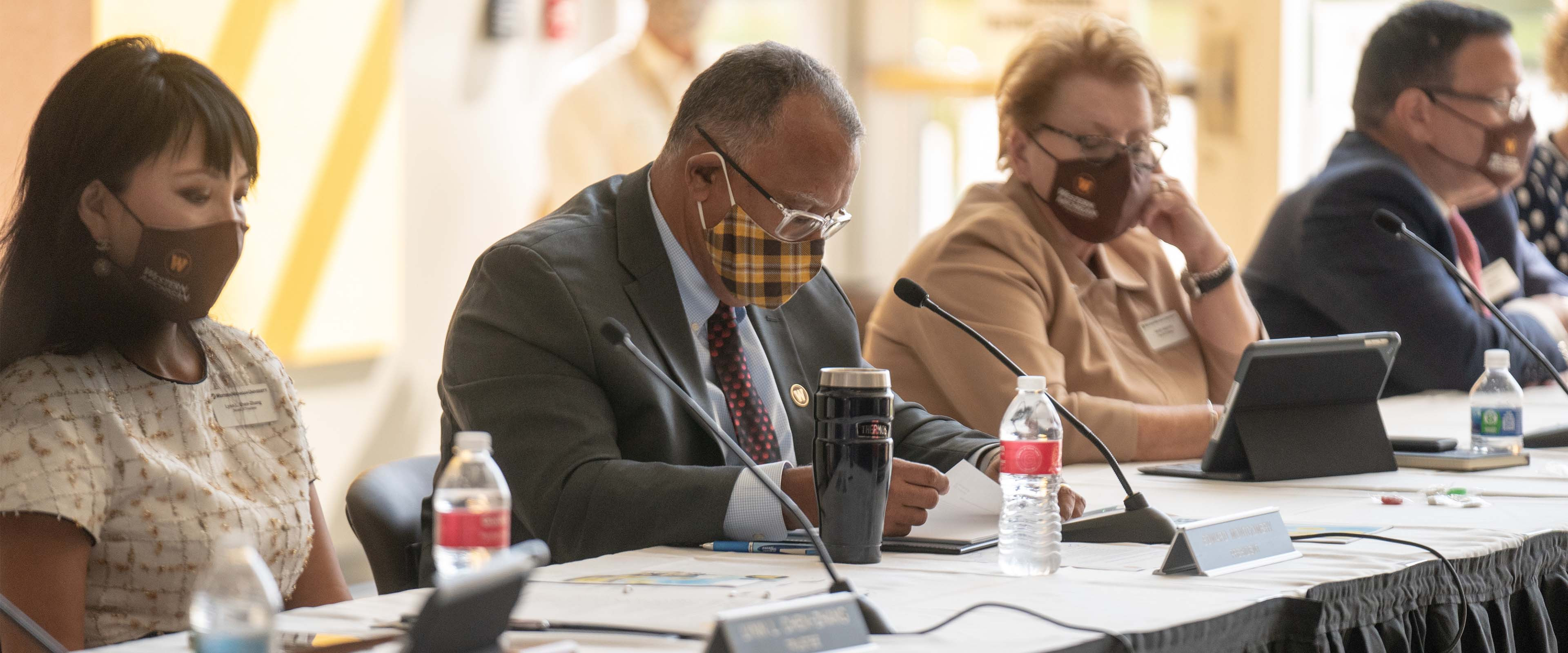 The Board of Trustees and President Edward Montgomery sitting at the board table in front of the microphone.