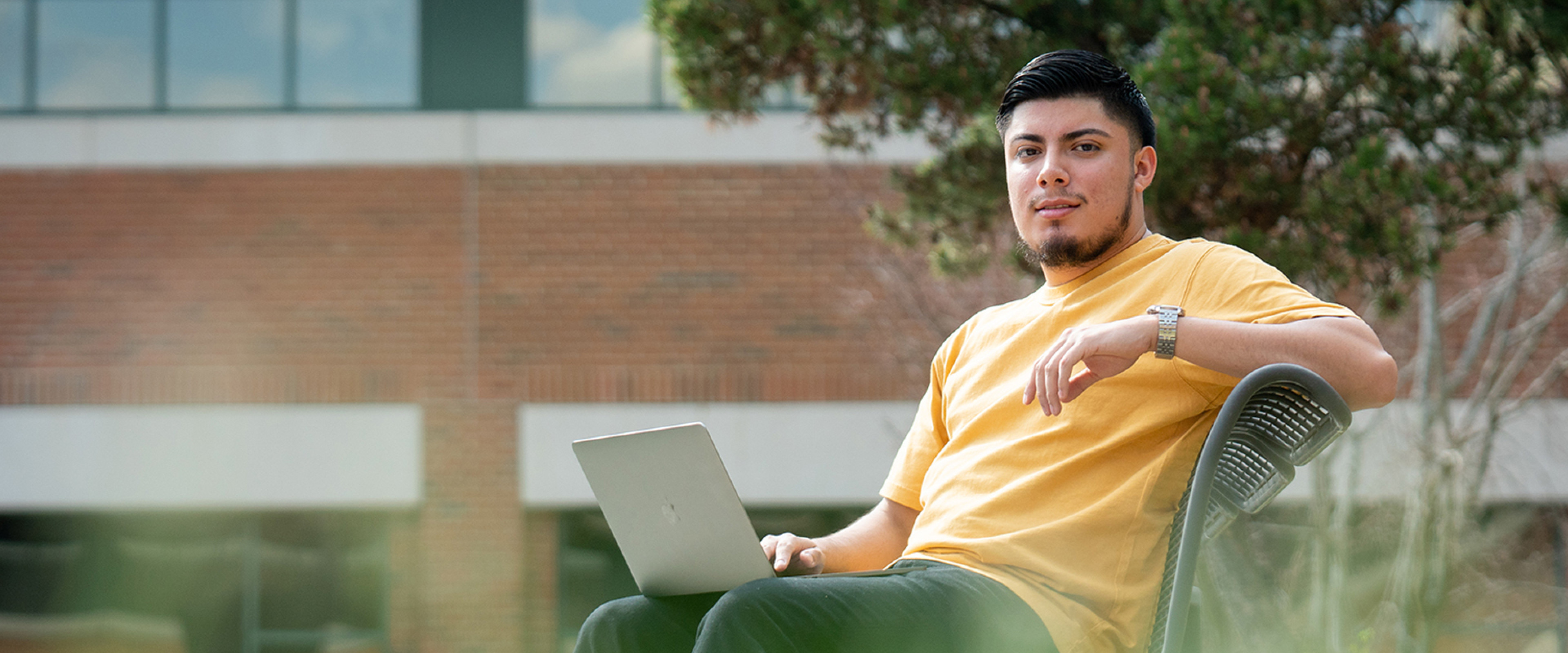 Male student on a bench with computer.