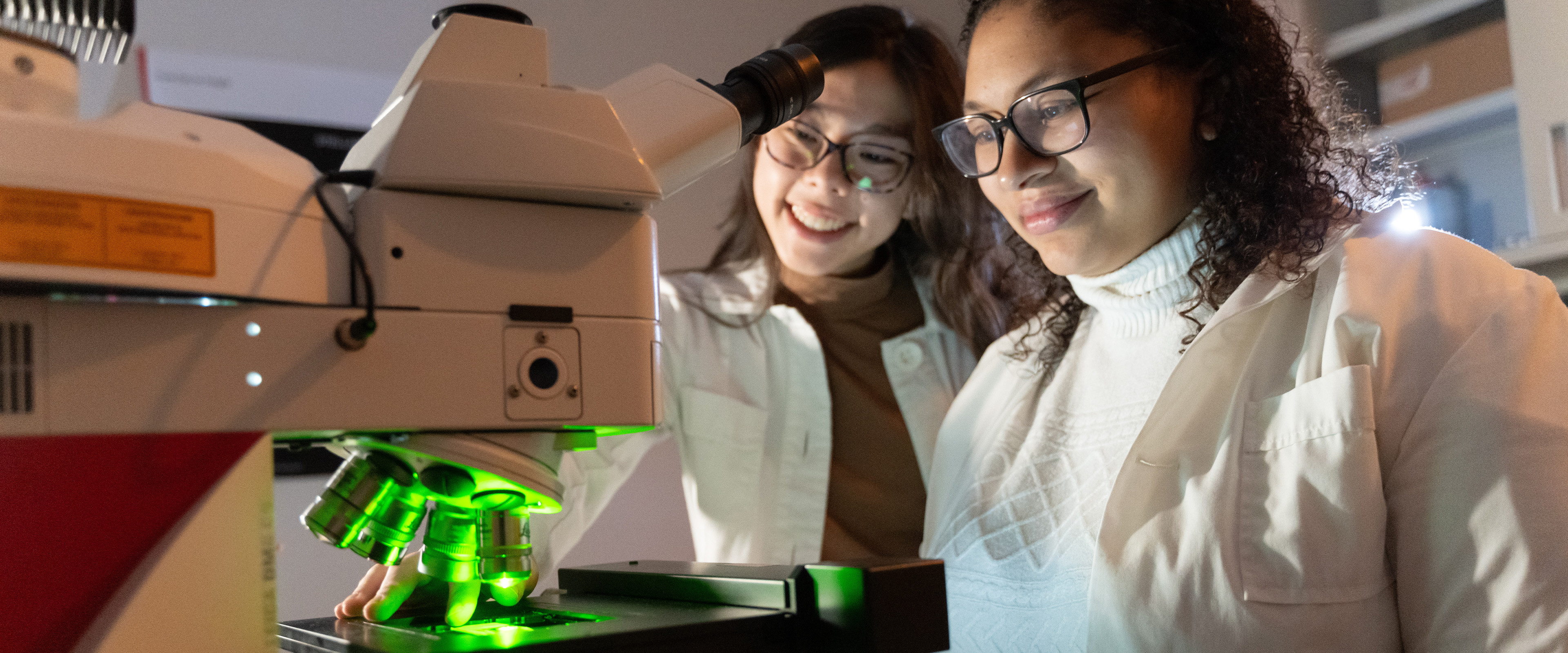 A student looking at a microscope with a professor.