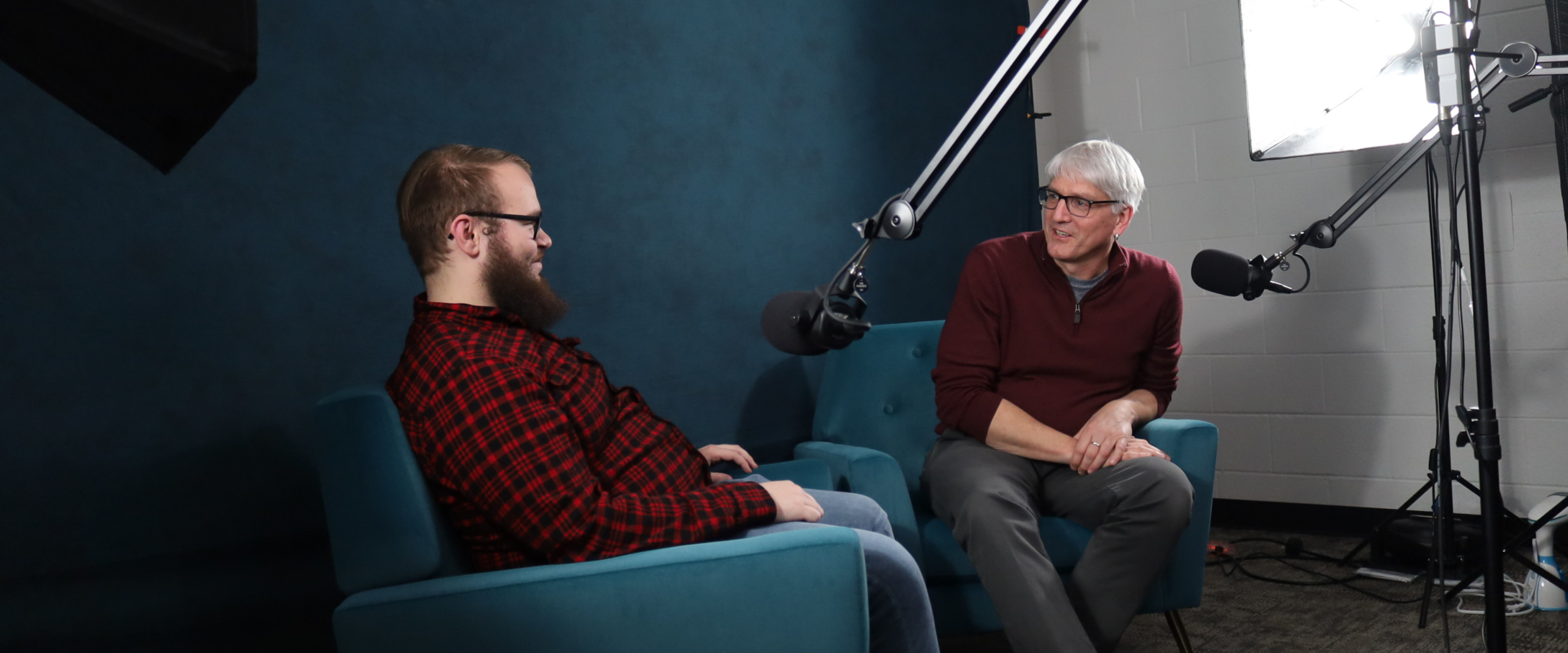 Two people seated in podcasting room.