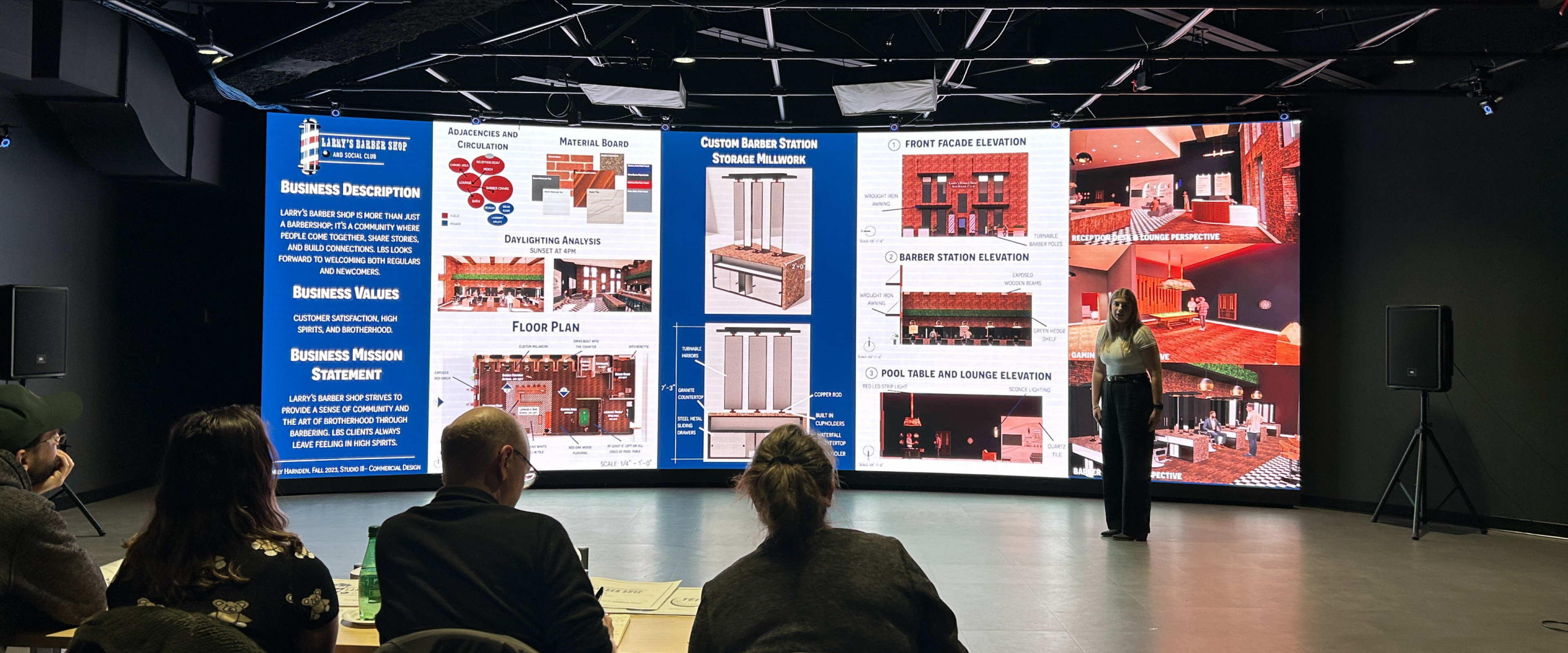 Interior designer showcases proposal on LED wall. Observers shown seated at tables for the presentation.