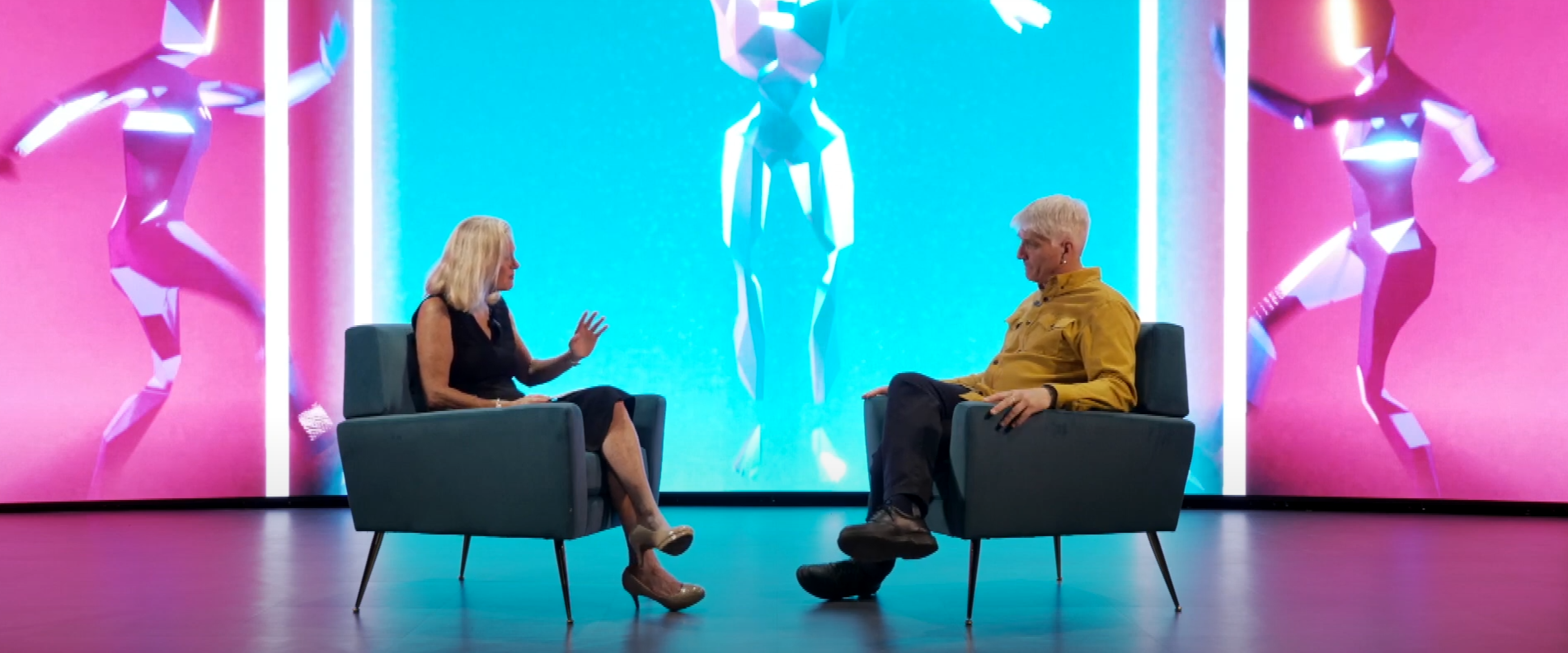 Two people sitting in chairs in front of LED wall for interview.