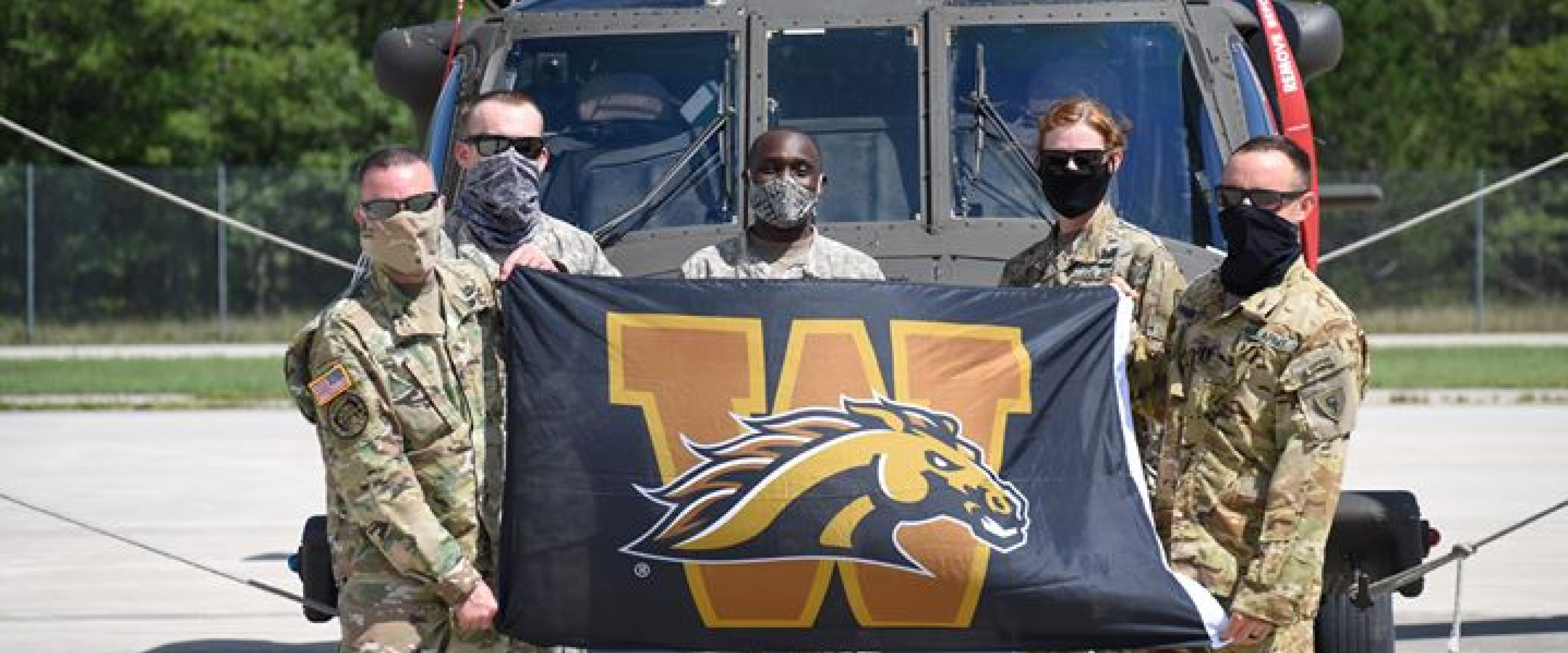 WMU military alumni holding a WMU flag in front of a helicopter
