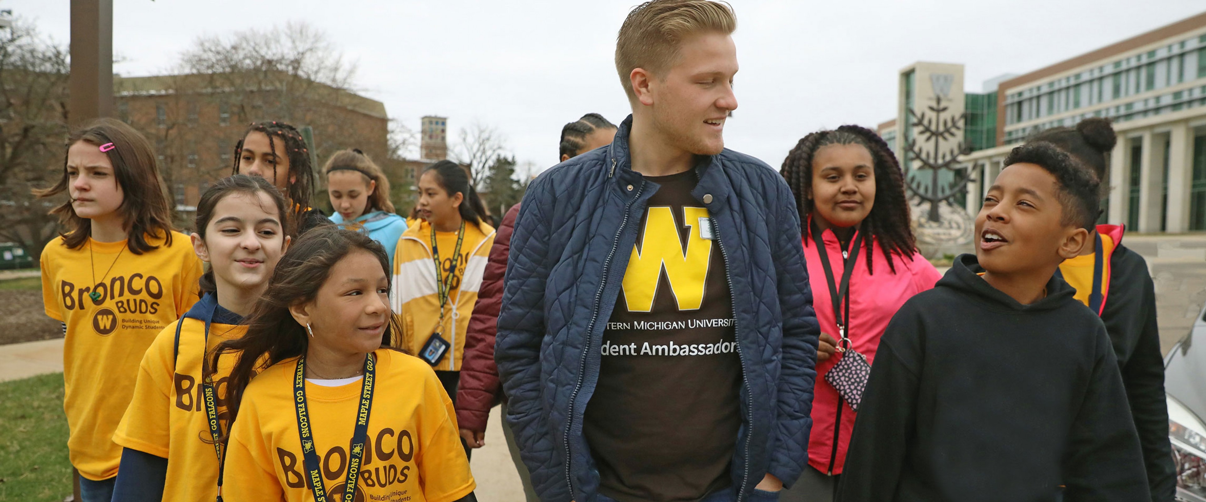 A student ambassador walks main campus with a diverse group of middle school students
