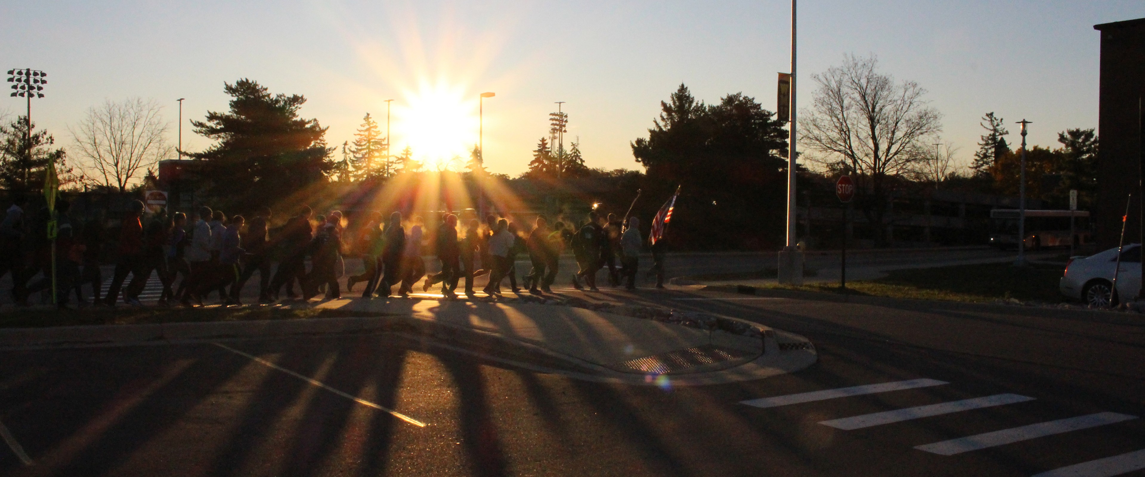 Students and staff participating in the Veterans Day Run. The sunrise causes the runners to appear as dark silhouettes, with only their breath being visible. 