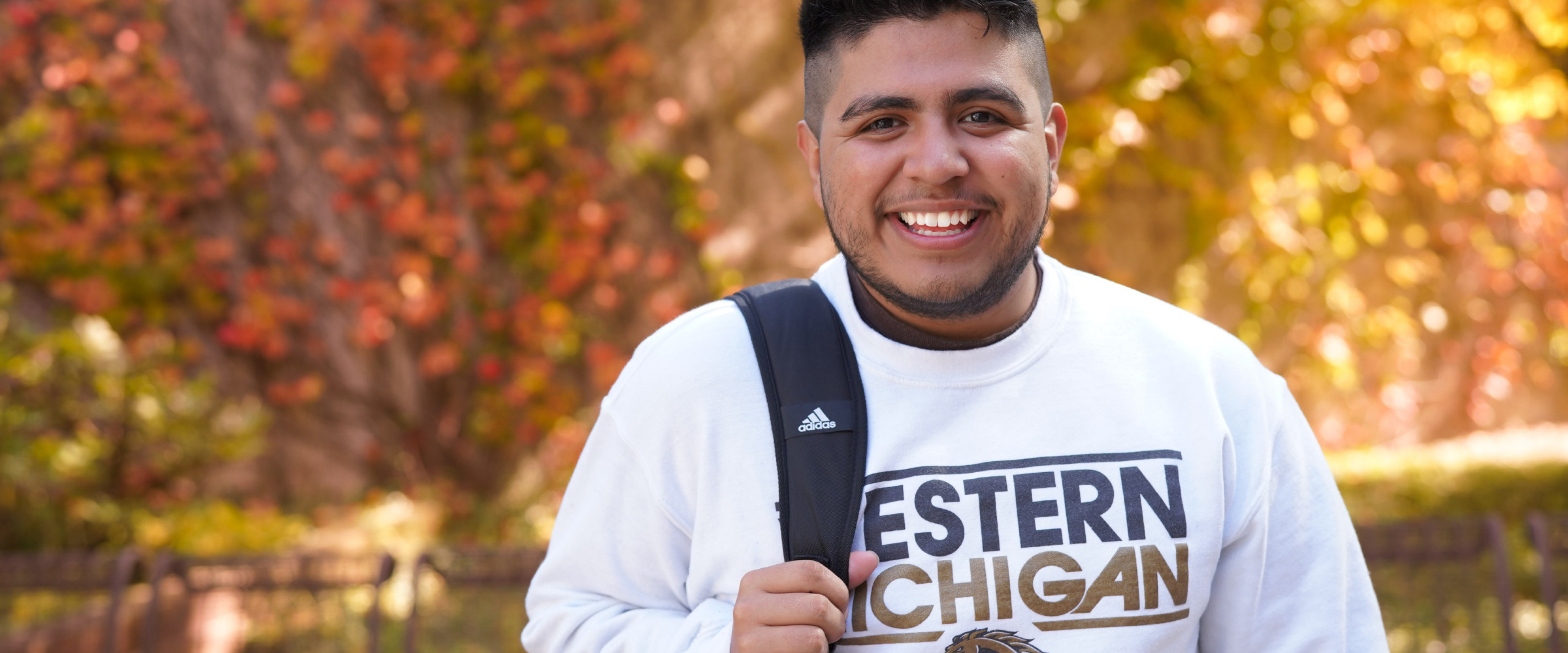 A student smiling on campus with fall foliage in the background