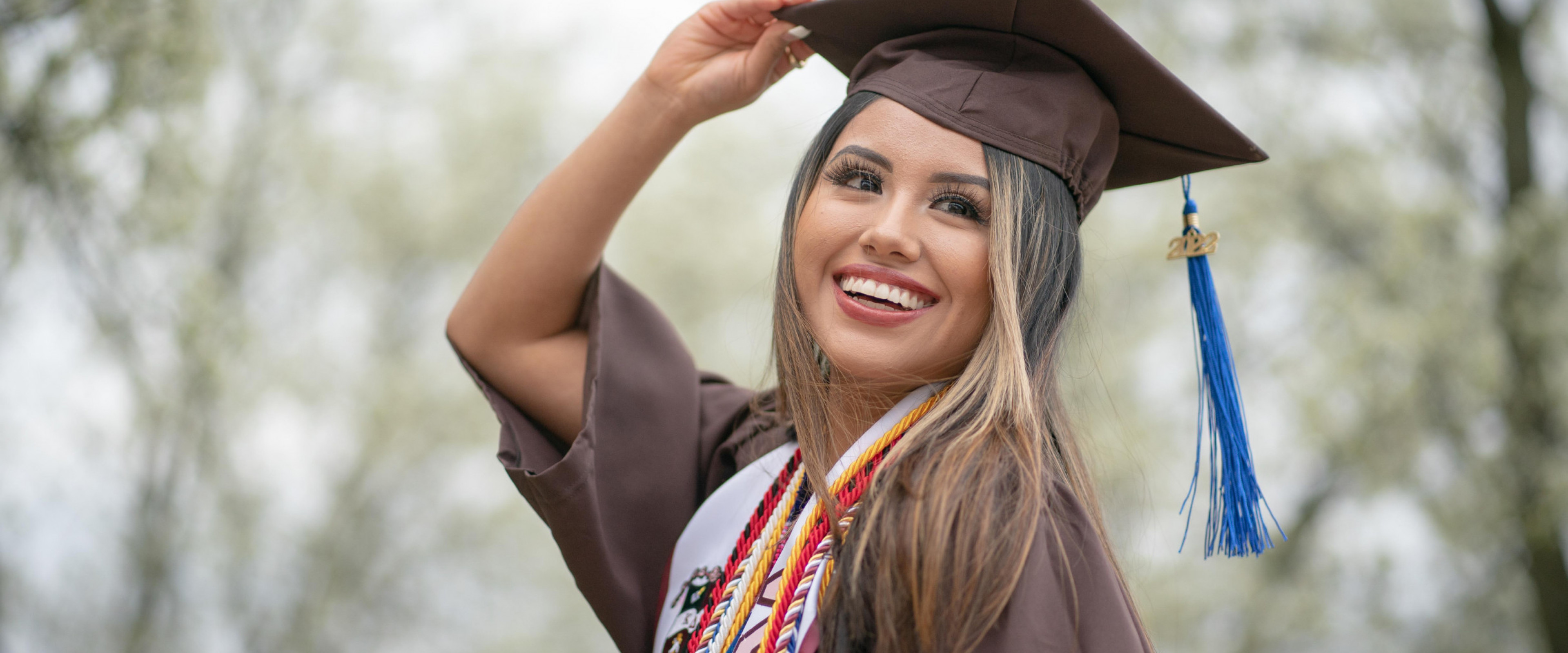 A smiling graduate wearing regalia and cords