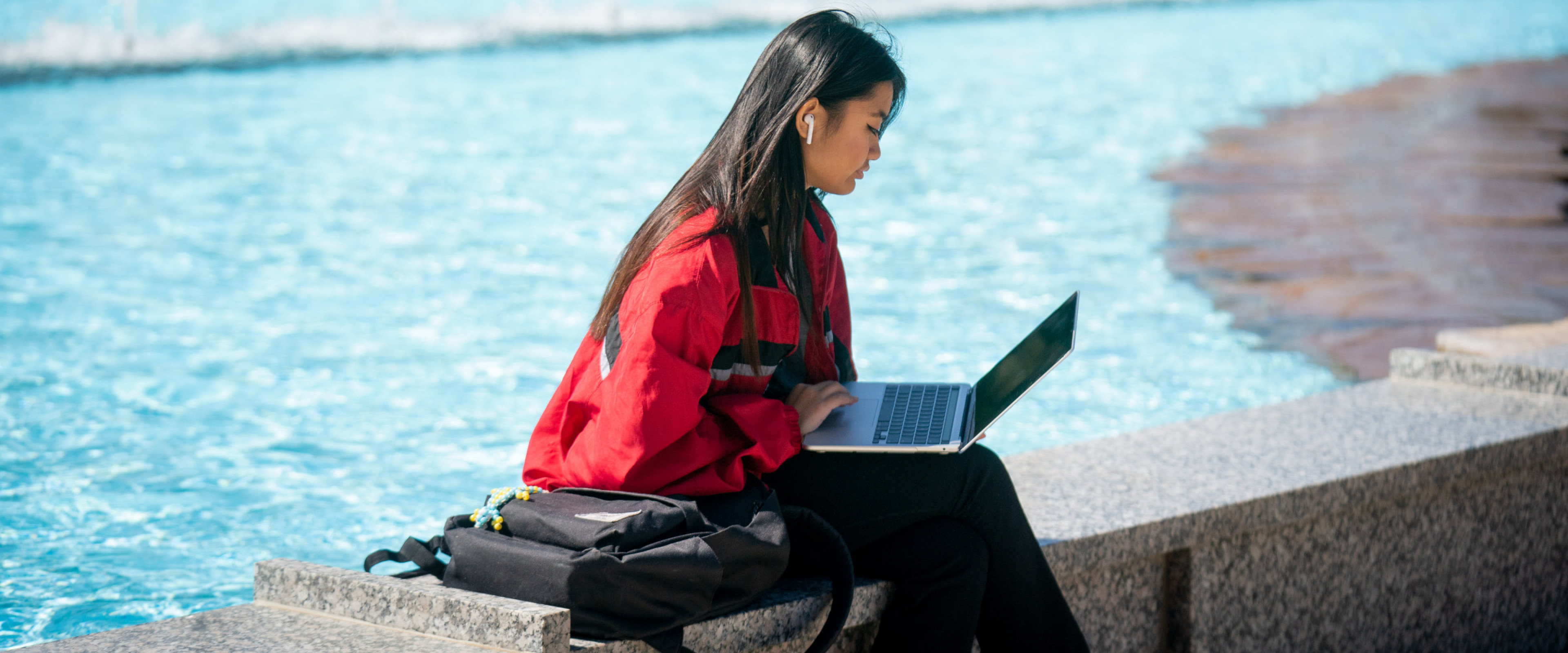 A student typing on a laptop at the edge of the Miller Fountain