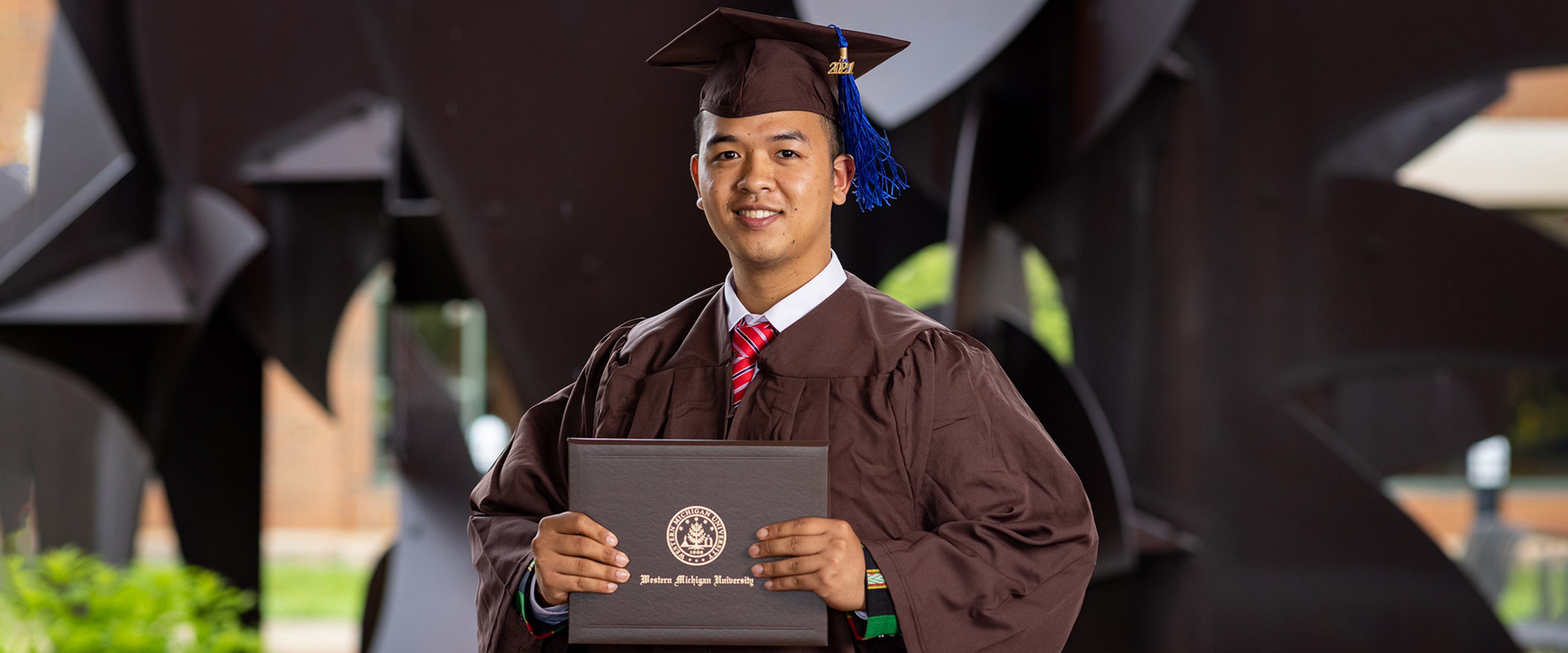 Student in cap and gown in Schneider Hall courtyard