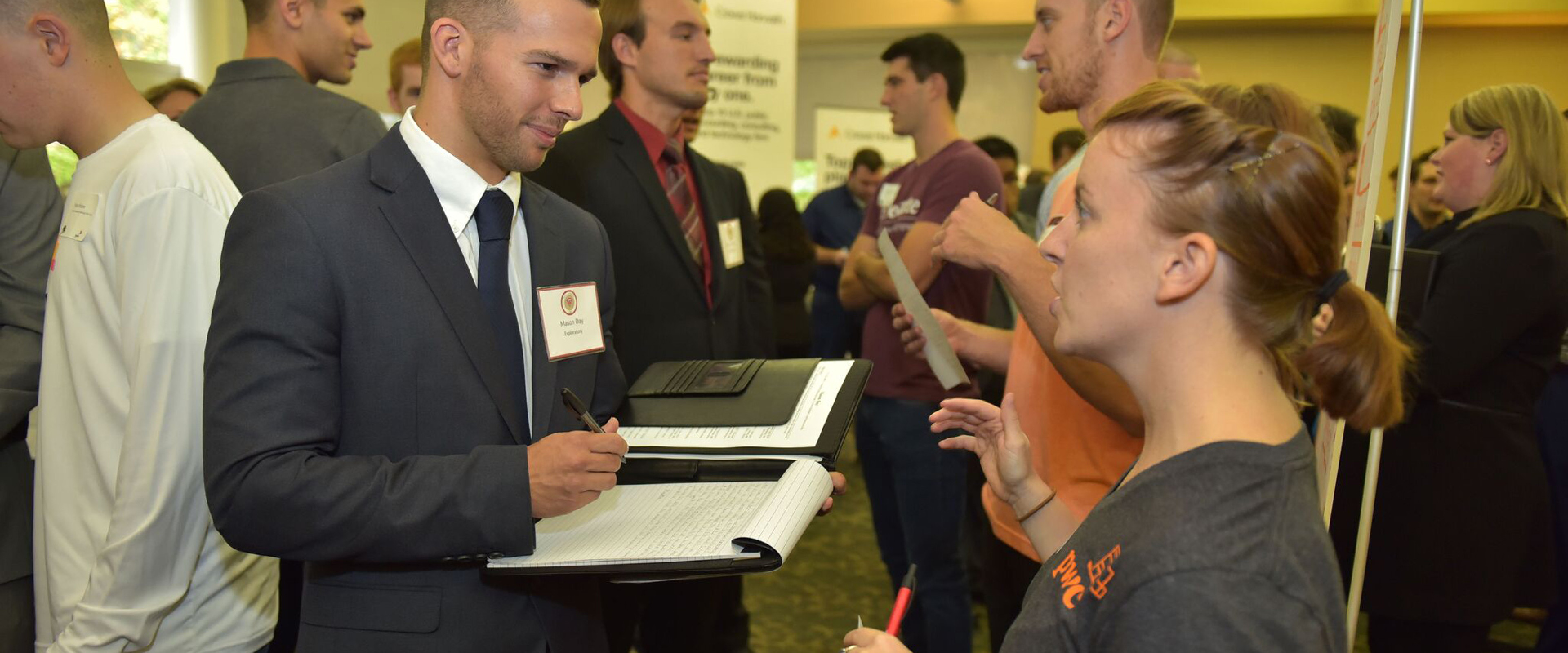 Student in professional dress speaking with a recruiter during career fair.