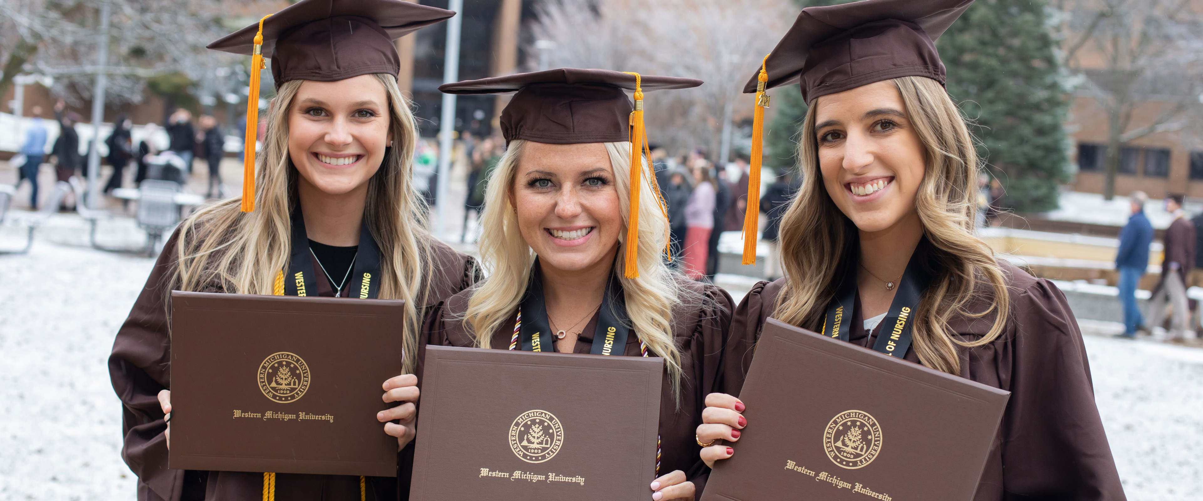 Three women in commencement robes and hats with engineering tassle