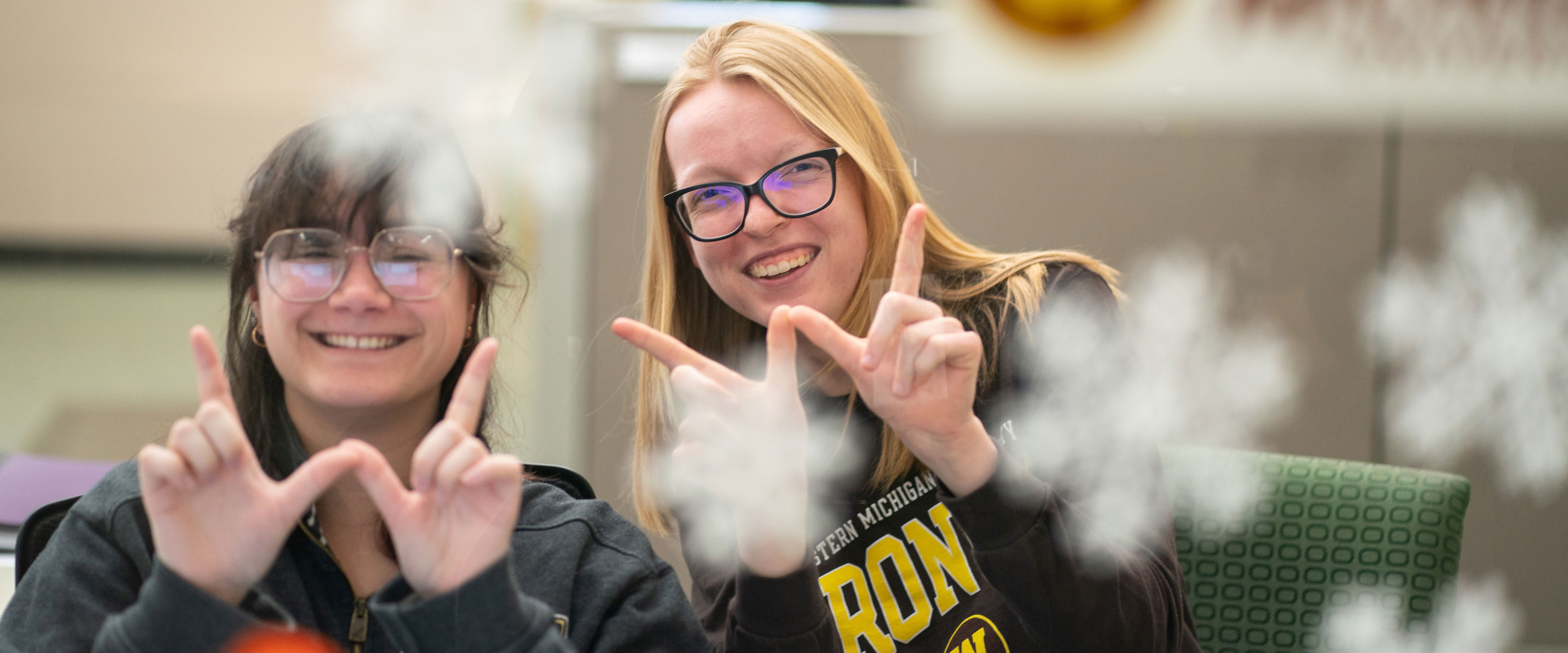 Two smiling students displaying a W formed with their fingers