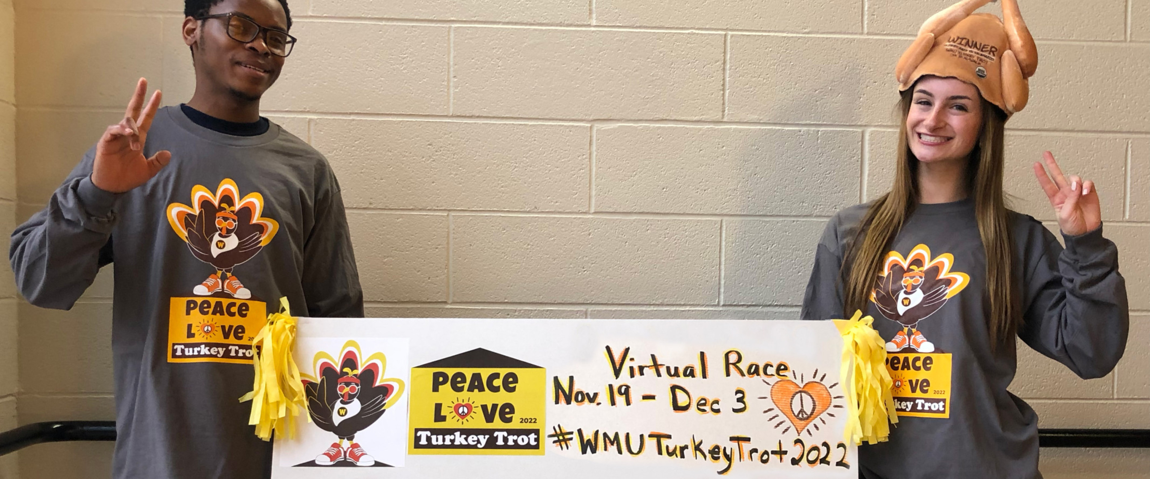 Two people holding a Virtual Turkey Trot sign wearing Turkey Trot T-shirts