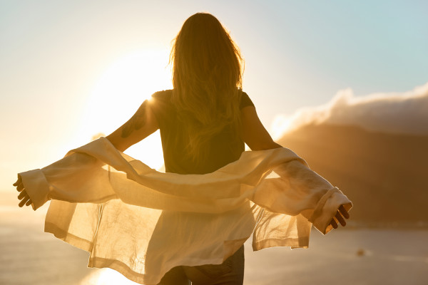person standing in front of a sunset with a shirt flowing in the wind and espressing the feeling of letting go.