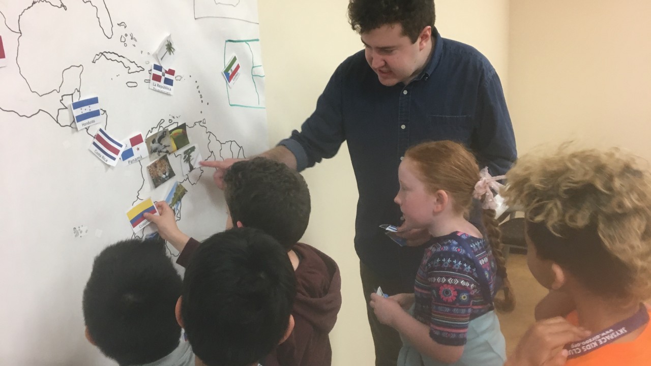 Mitch Barrett points to a map on the wall helping third graders identify countries on the map