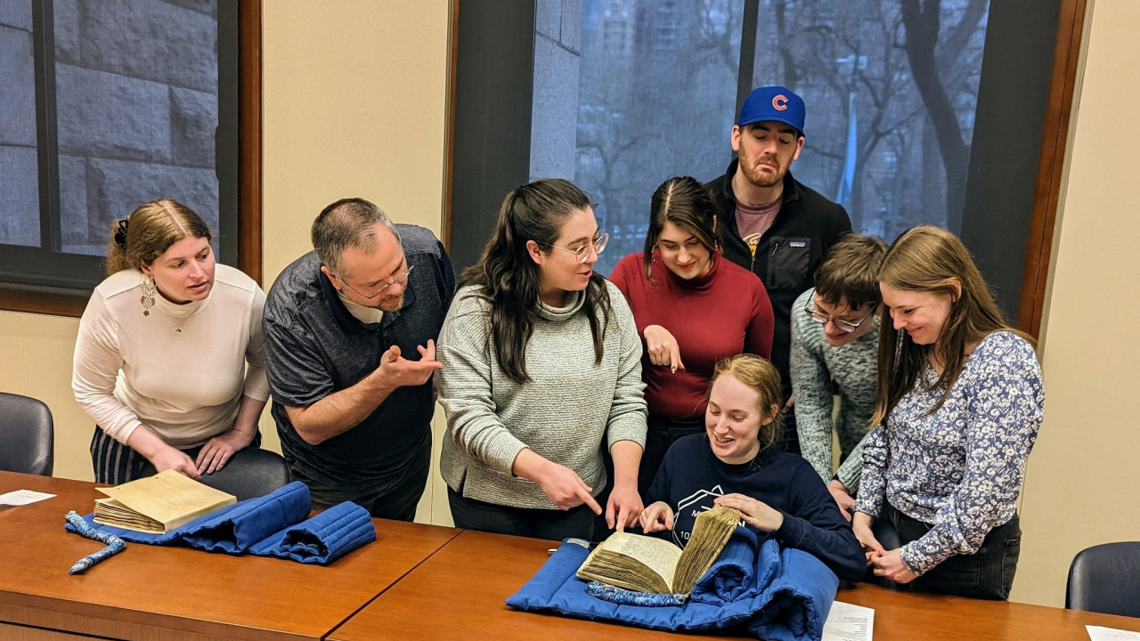 A group of students clustered around medieval manuscript