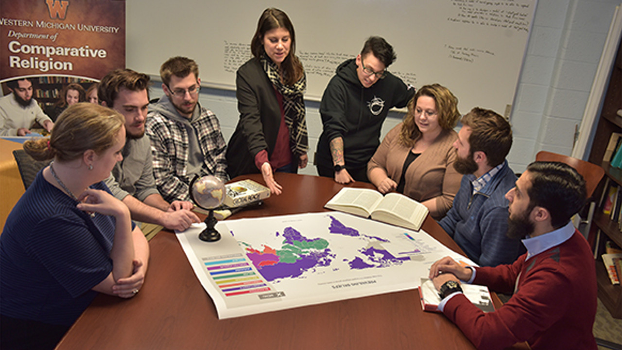 Seven students at table with faculty member looking over world map of religious regions