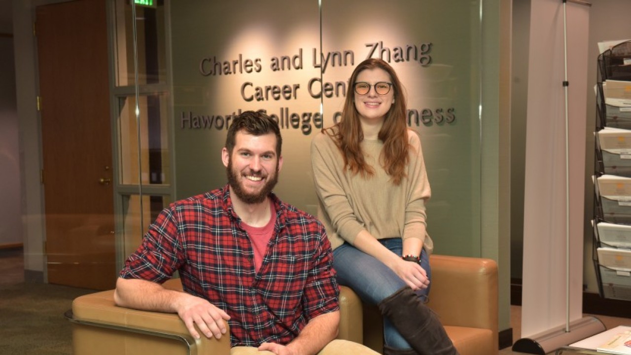 Two smiling students sitting in career center in front of Zhang Career Center sign.