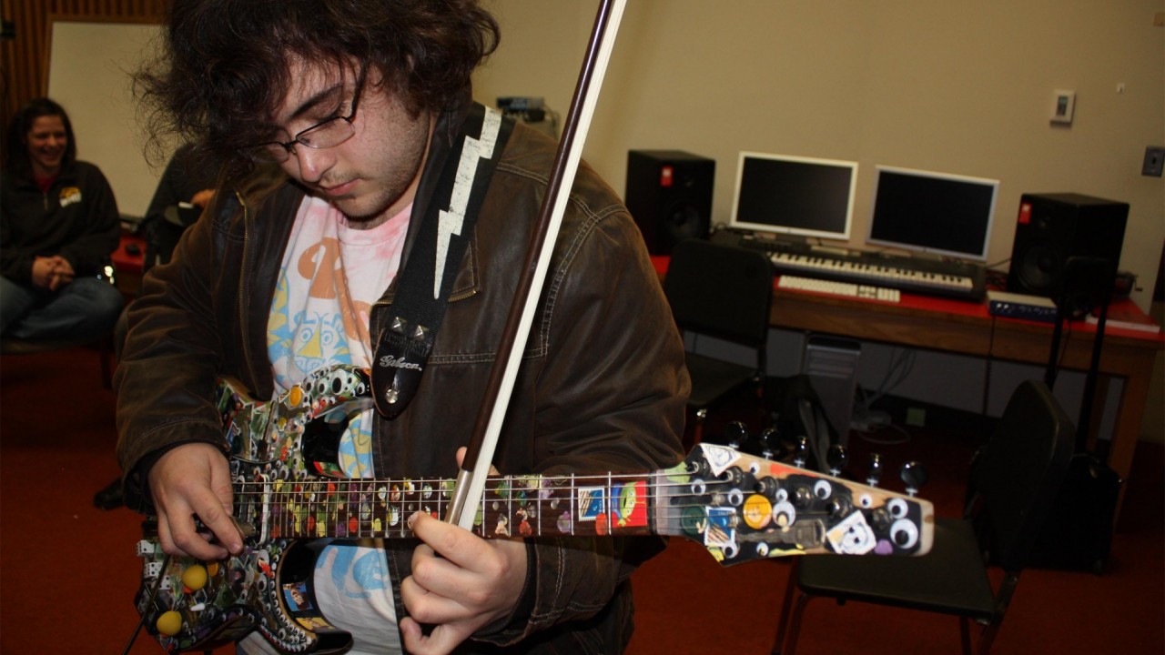 Photo of a student playing electric guitar with a bow.