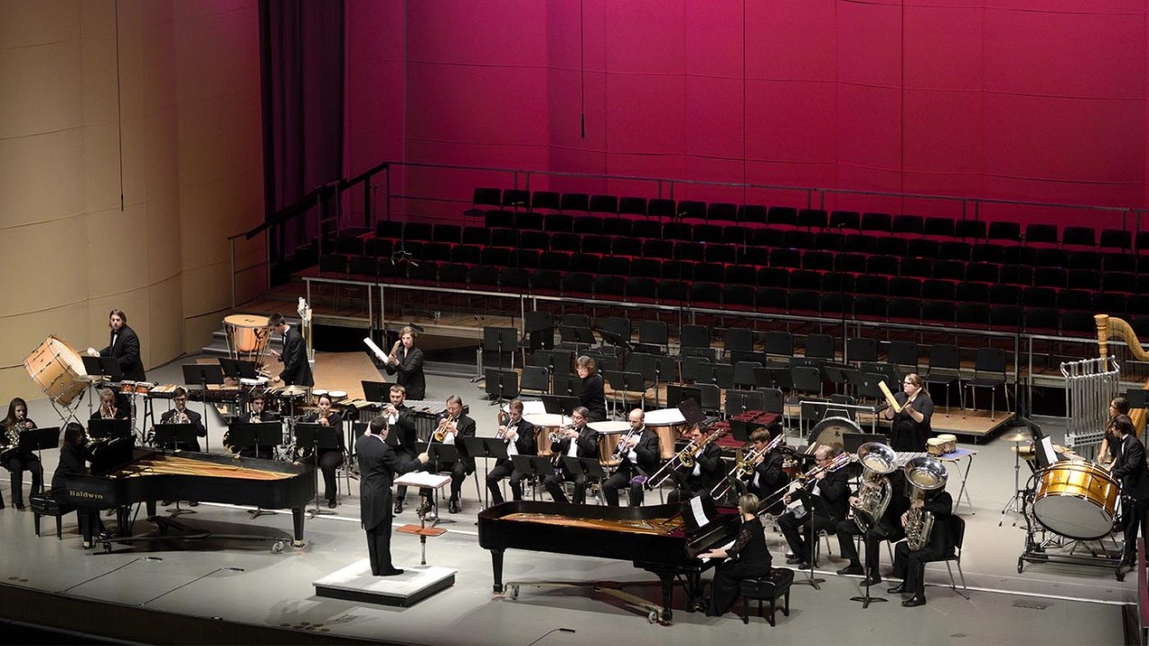 Photo of a chamber wind ensemble performing on Miller Auditorium's stage with red back lighting