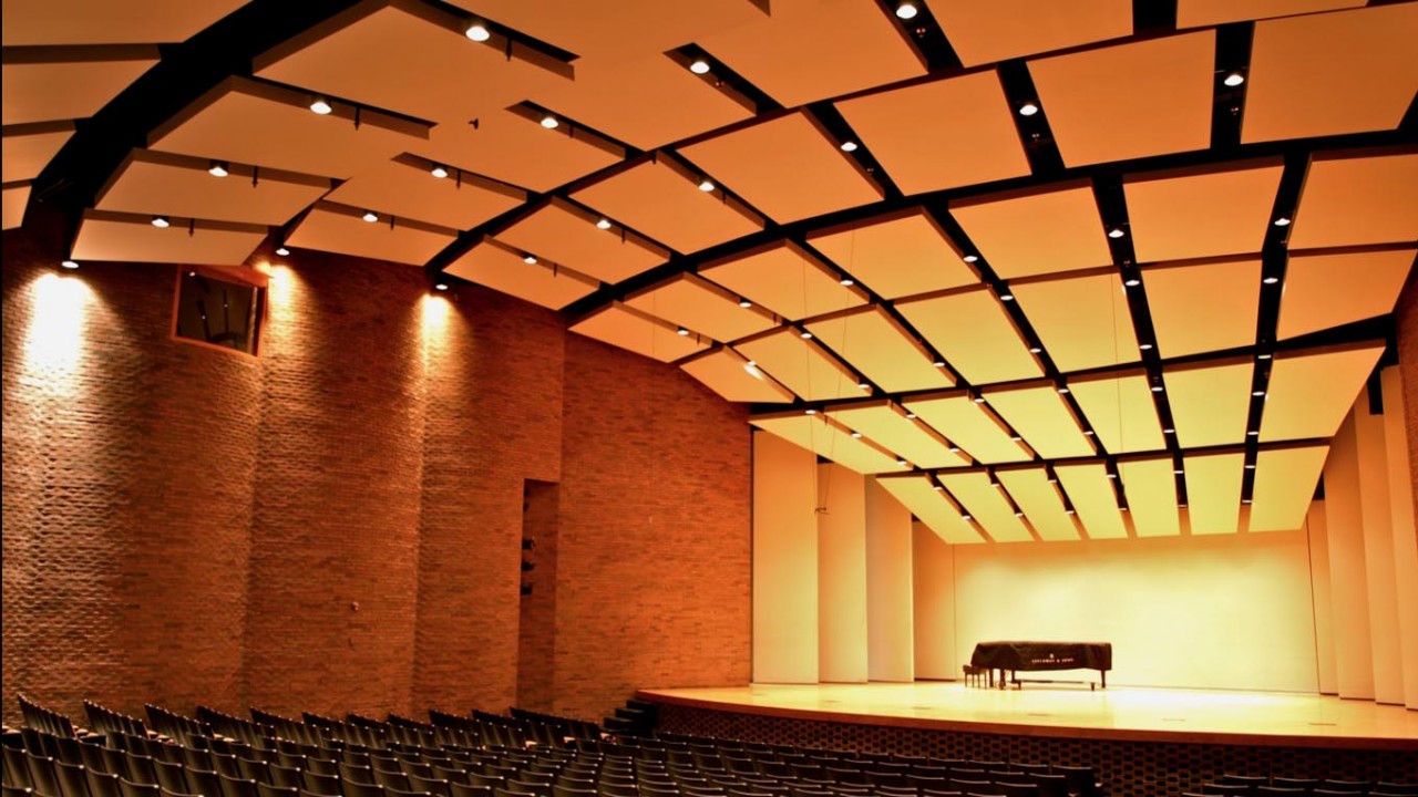 Photo of the recital hall with a grand piano center stage with an empty audience
