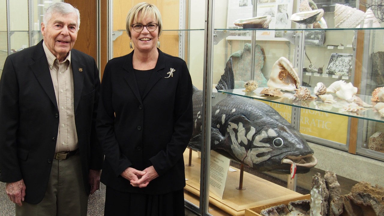 Museum founder and a former student stand next to a coelacanth exhibit