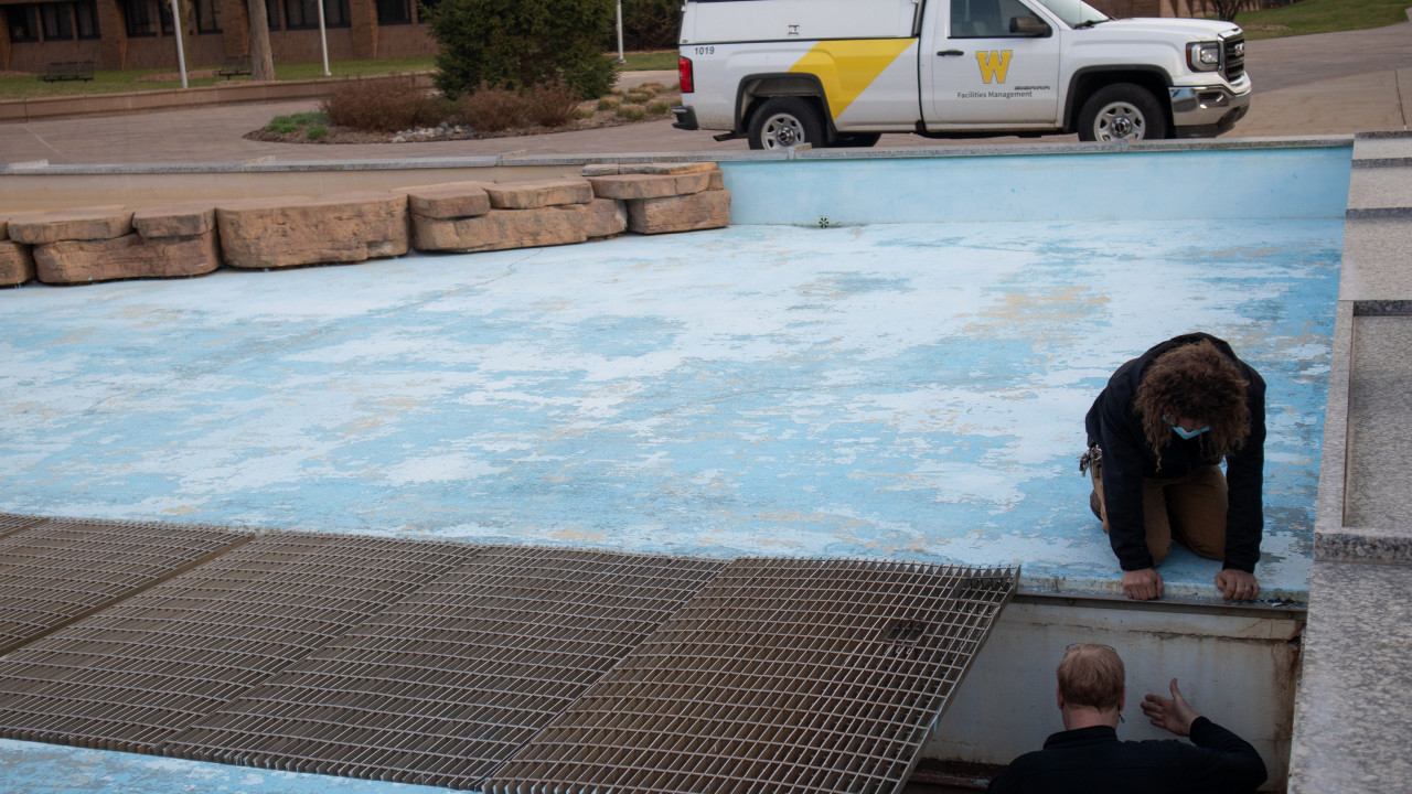 Photo of two employees inside the Campus fountain, looking into the pit area under some grates with a maintenance truck in the background
