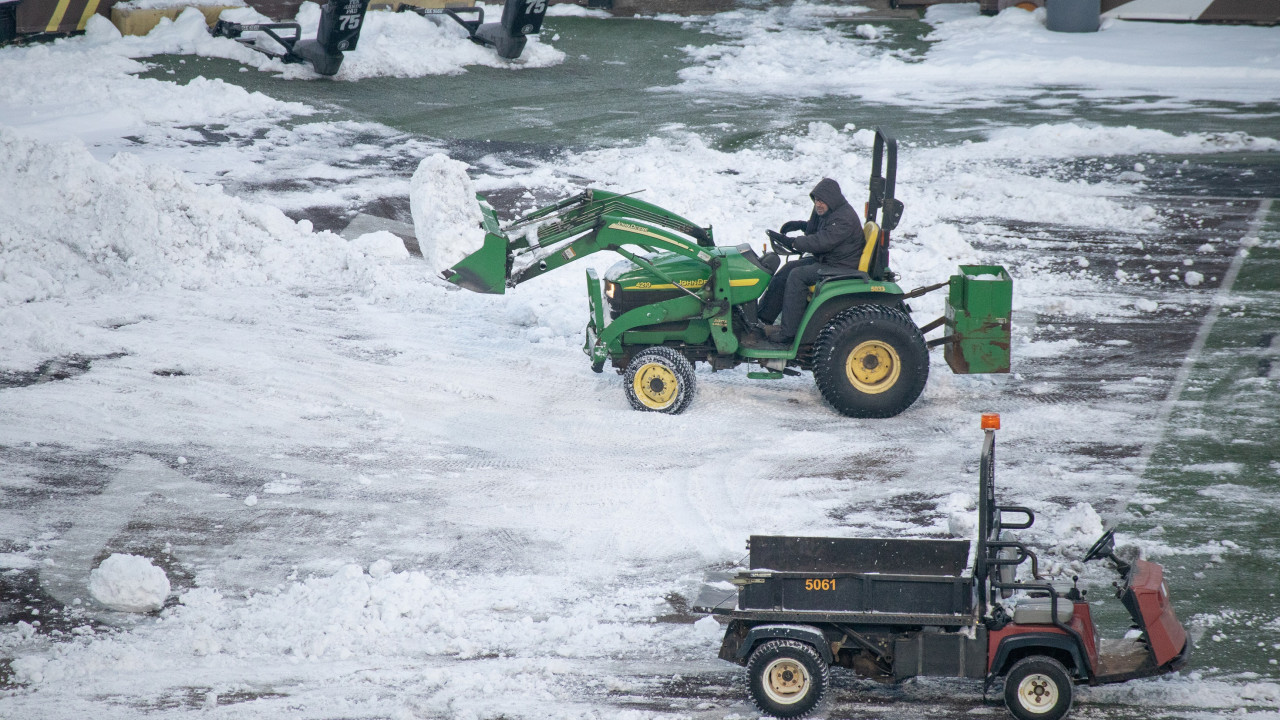Landscape employee uses John Deere tractor to move snow on football field surface.
