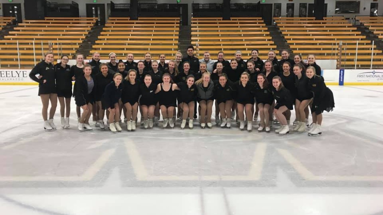 Skating club team photo. Entire time in black wearing their skates and on the ice posing together with coaches