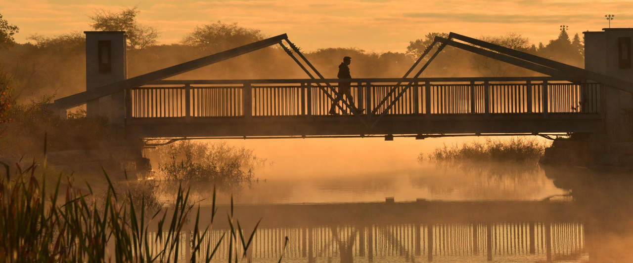 silhouetted figure walking across Goldsworth Pond bridge on a foggy morning