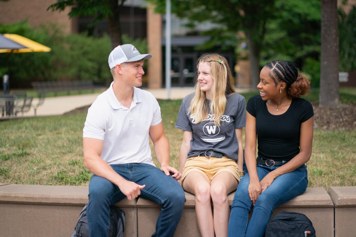 Three students sitting on campus, near the fountains. 