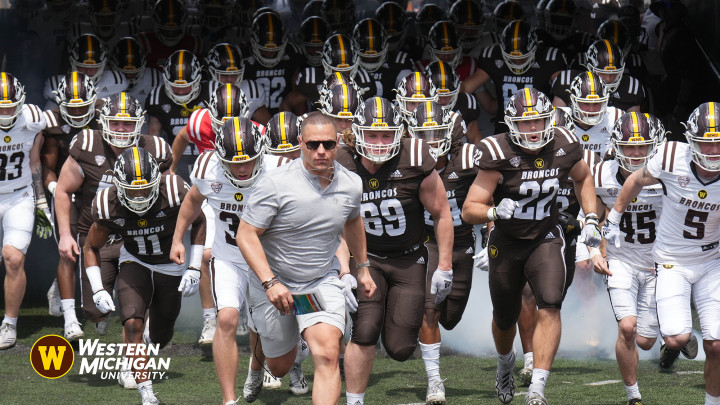 Photo of the football team, coach in front coming out of the tunnel. #WMU2024GRAD