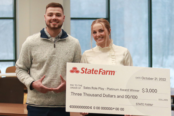 Two students in the sales and business marketing program, hold a plaque and a giant check for placing second at the State Farm Marketing and Sales Competition.