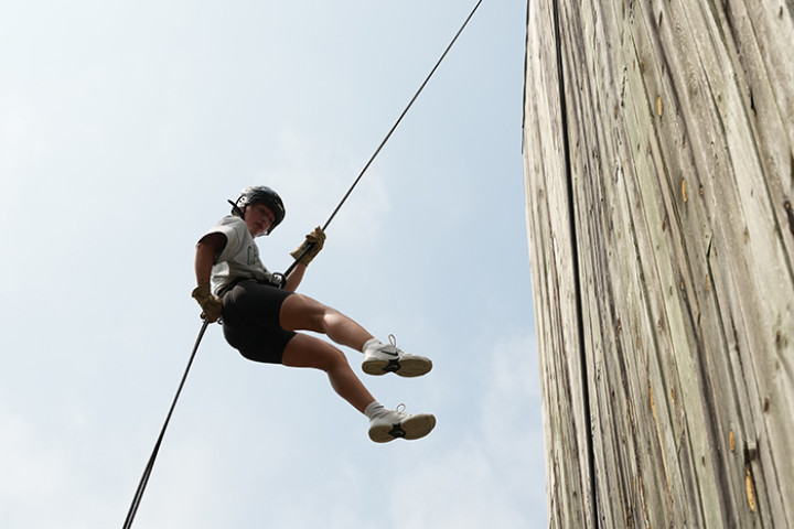 Student repelling down from a wooden tower.