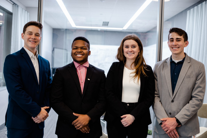 Four students, dressed in business professional attire, pose with their hands crossed.