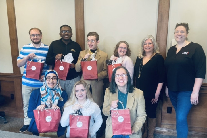 9 students and Heather Isch of LFK Marketing hold red gift bags.