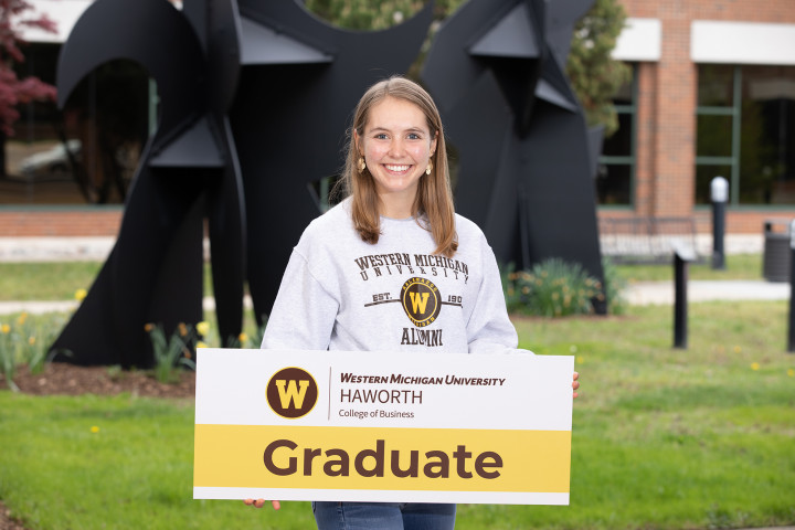 Alexis Hess, an accountancy student, holds a sign that says Graduate with the WMU Haworth logo.