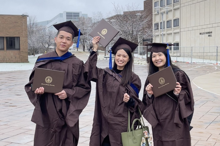 Three Taiwanese MBA students, dressed in their graduation caps and gowns, are outside celebrating.