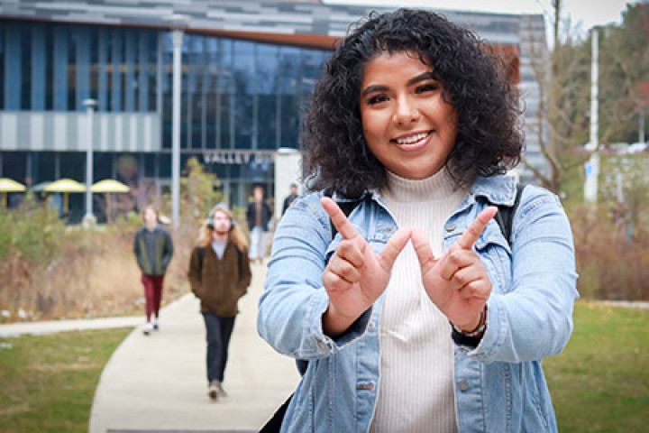 Michelle Herrera is standing outside of the Valley Dining Center, with their fingers making the shape of a 'W.'