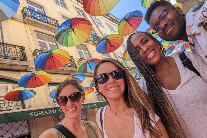 Four MBA students are standing under rainbow umbrellas in Portugal.