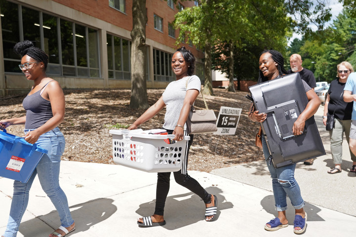 Students and families moving hampers and a TV into a residence hall room.