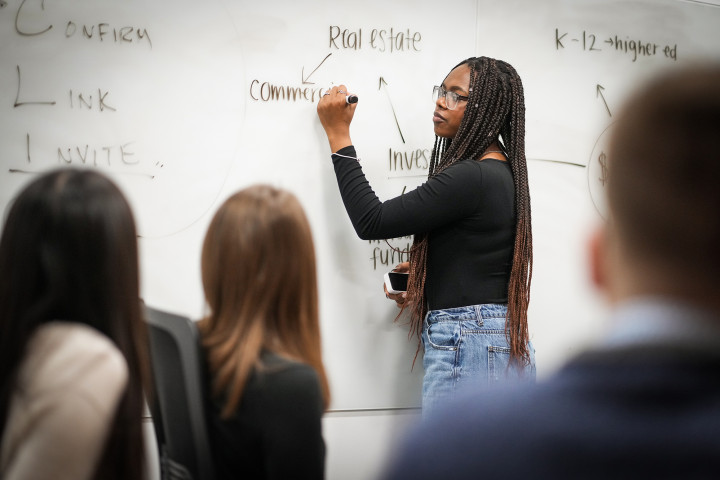 Student at the Haworth Business College at a white board with other students looking on.