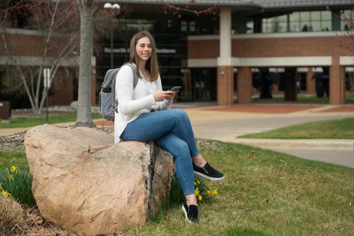 Female student sitting on a rock, posing, outside of the Haworth College of Business