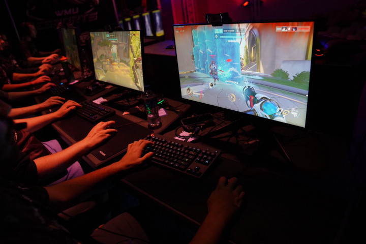 The hands of esports players rest on keyboards in front of a computer monitor.