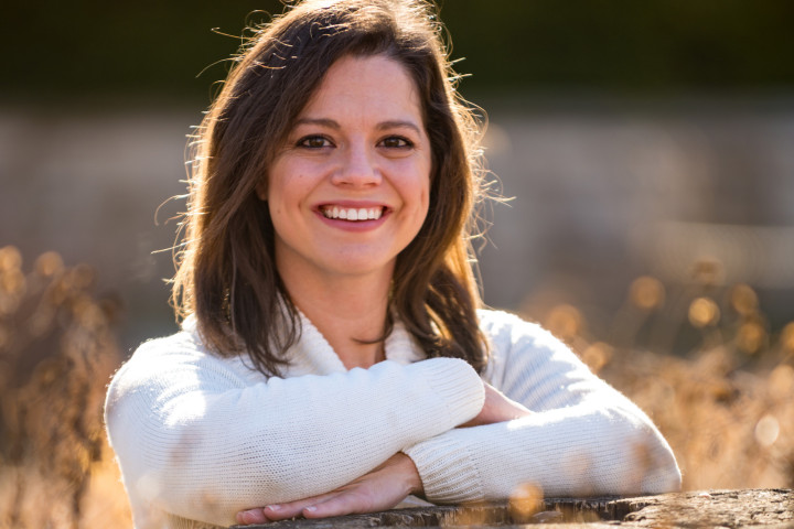A portrait of Dr. Traci Brimhall leaning on a tree stump in an outdoor setting.