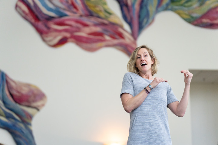 Kate Thomsen instructs a class in front of a colorful wall.